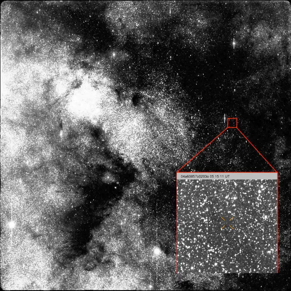A grainy black and white field of the Milky Way with a red box marking a tiny point, enlarged in an inset.