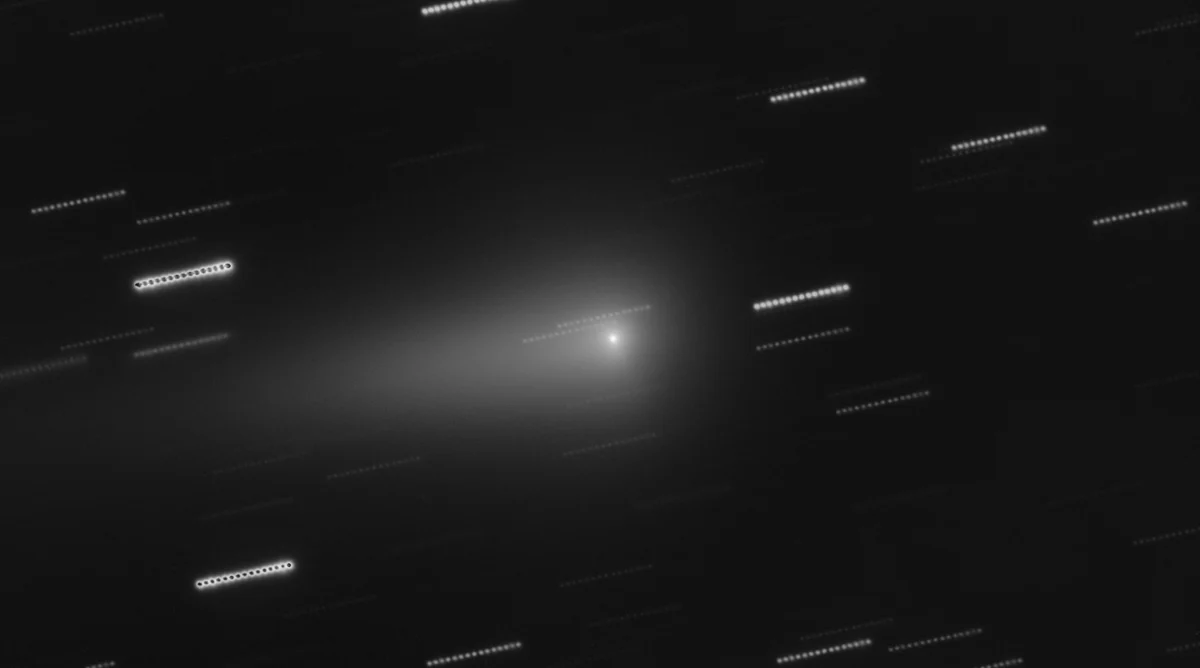 A grey comet with a bright core and a long faint tail among streaked stars, photographed by the Very Large Telescope.