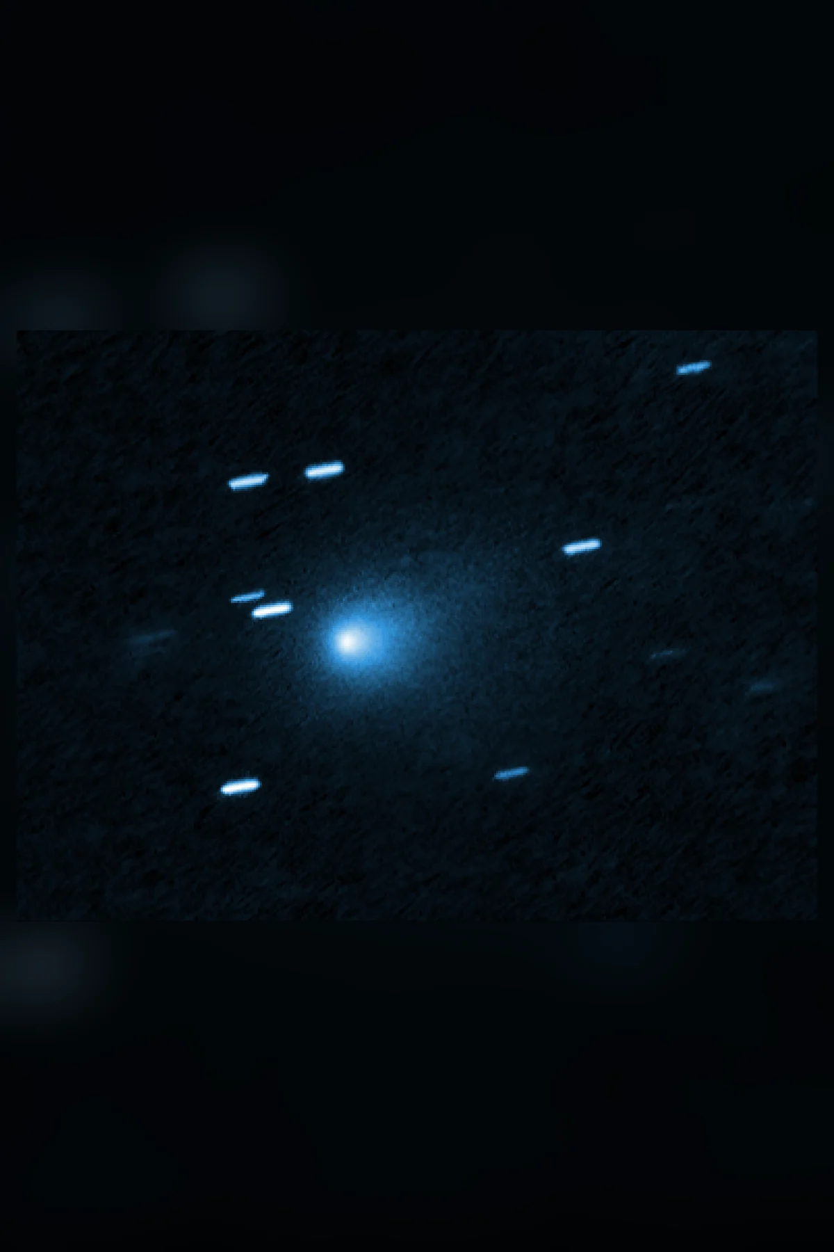 A small blue-white comet with a teardrop-shaped glow of dust, among short streaks of stars, set on a darkened, blurred copy of the same photograph.