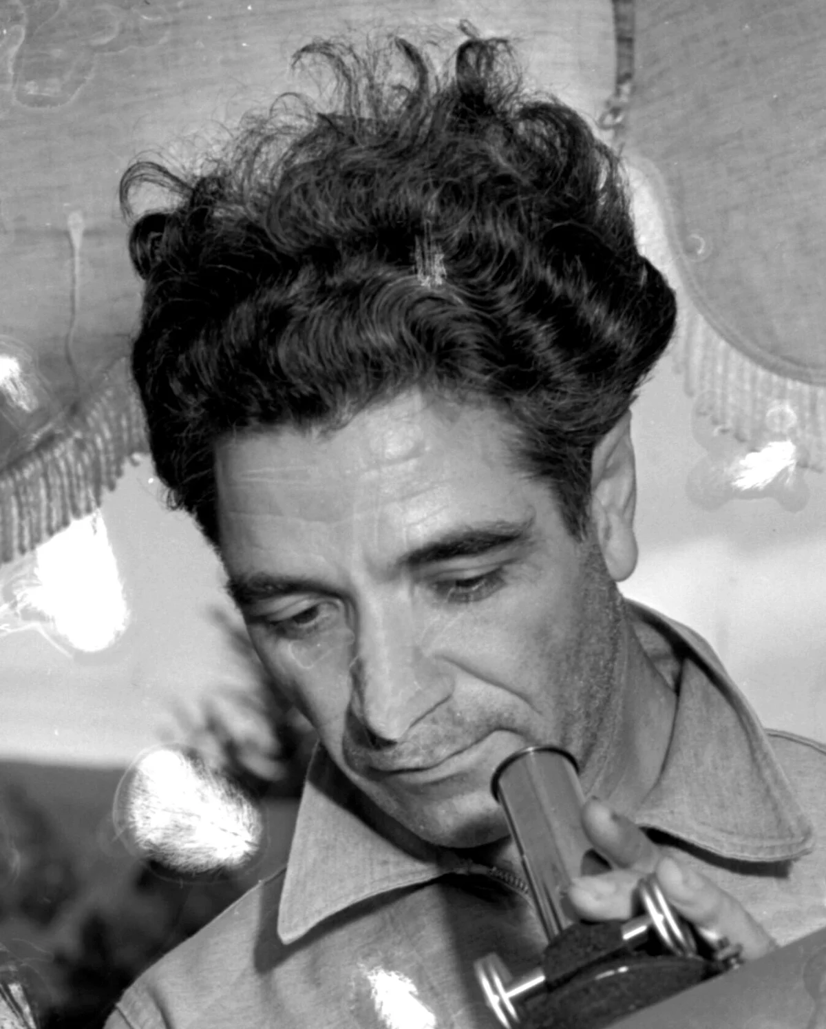 Black and white photograph of George Adamski, a dark-haired man in a work shirt, looking down into the eyepiece of a telescope.