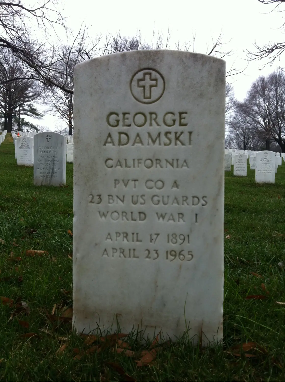 A white government headstone on green grass reading George Adamski, California, Pvt Co A 23 Bn US Guards, World War I, April 17 1891, April 23 1965.