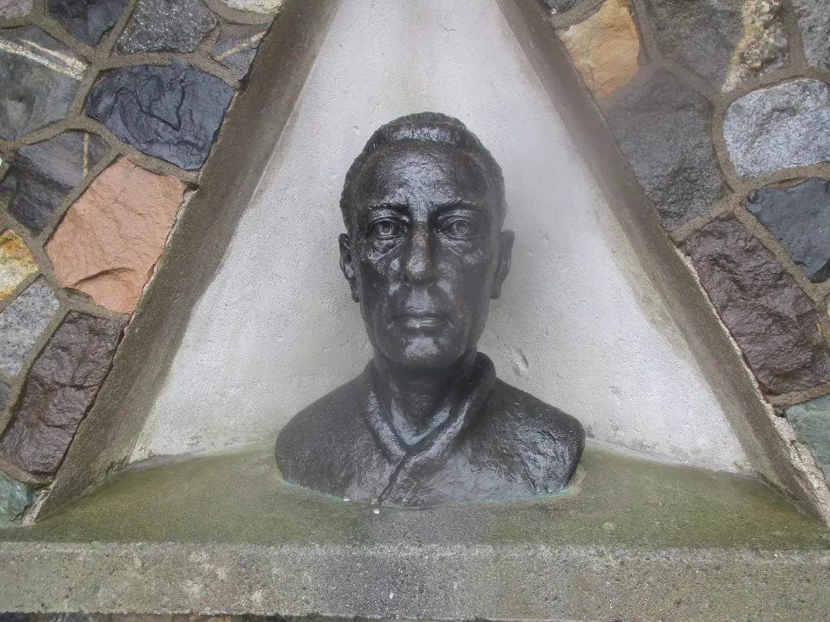 A dark bronze bust of a man set in a white triangular niche in a wall of coloured stone.