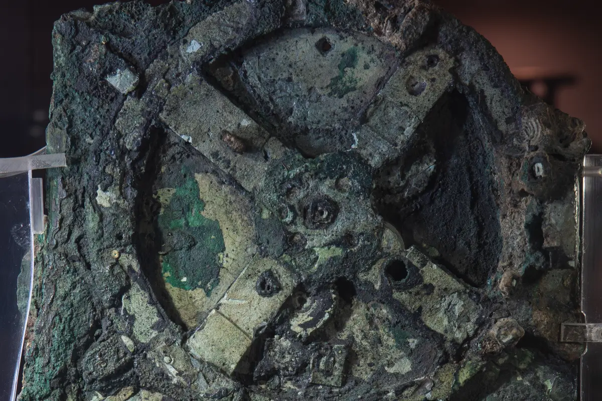 A close view of corroded bronze showing a large wheel with four broad spokes, holes and small raised stumps on them.
