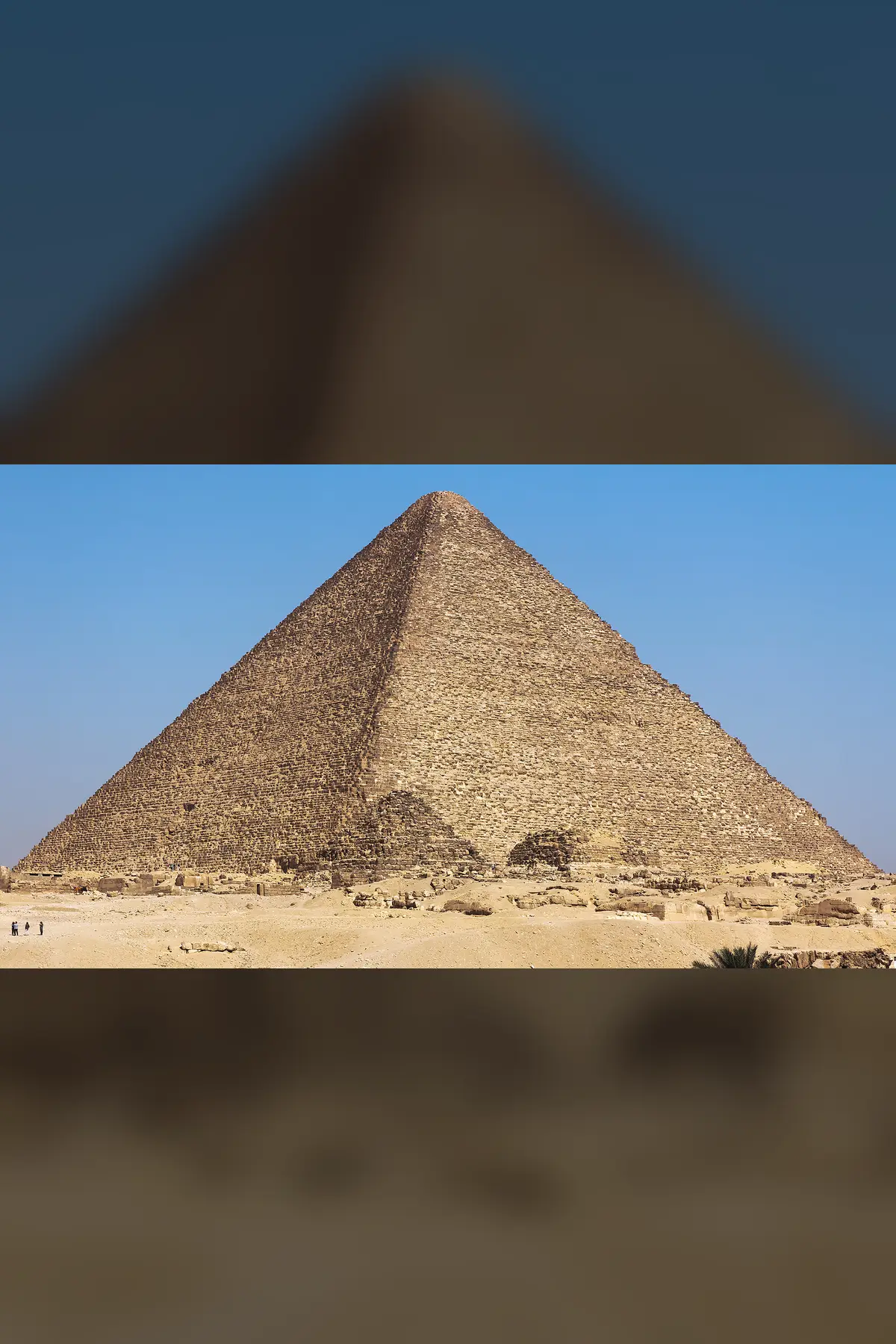 The Great Pyramid of Giza seen near a corner against a blue sky, with small queens' pyramids at its foot.