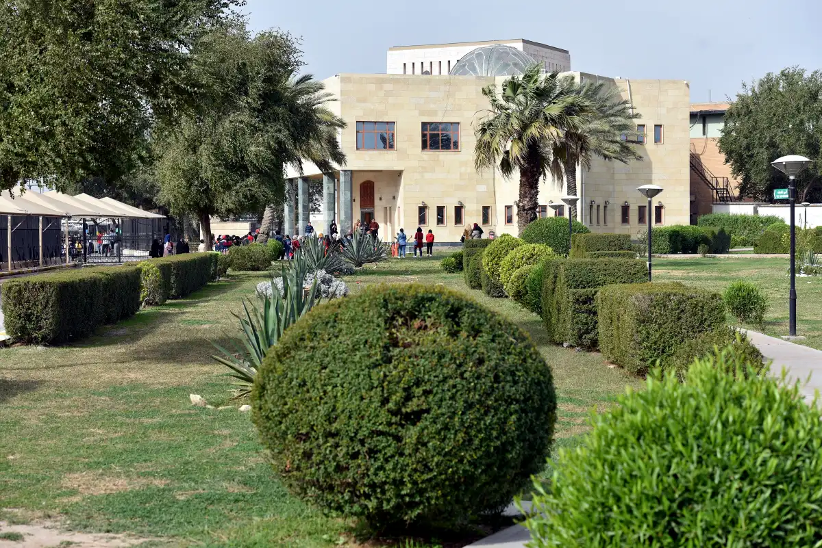 The garden courtyard of the Iraq Museum in Baghdad: clipped shrubs, palms and lawns in front of the pale museum building.