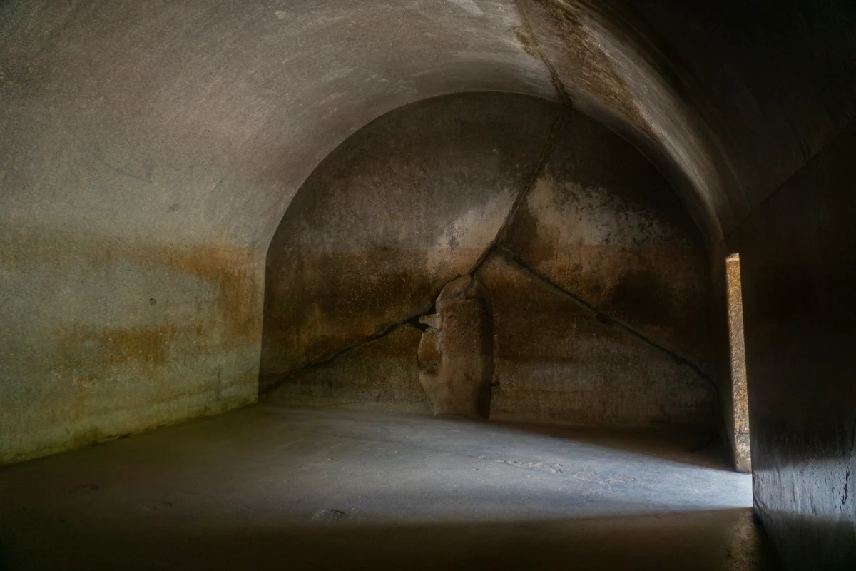 The inside of the Sudama cave: a smooth vaulted hall, lit from a side door, with the curved outer wall of the round inner chamber and its doorway at the end.