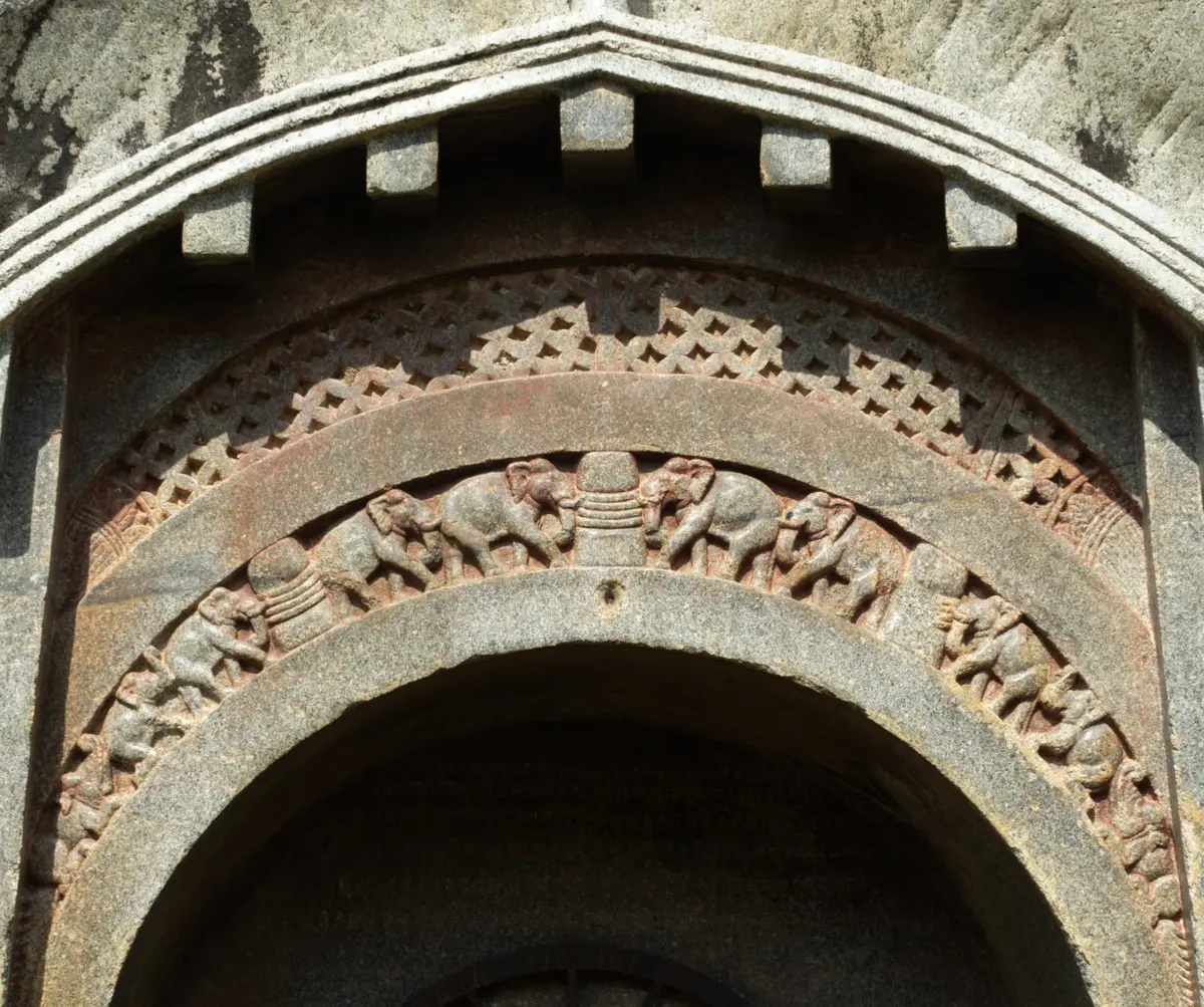 The carved arch over the Lomas Rishi door: beam ends above, a band of lattice, and a row of elephants walking along the curve toward a stupa-like shape.