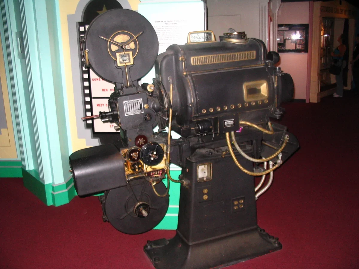 Mechanical motion-picture projector with film reels and a projection lens.