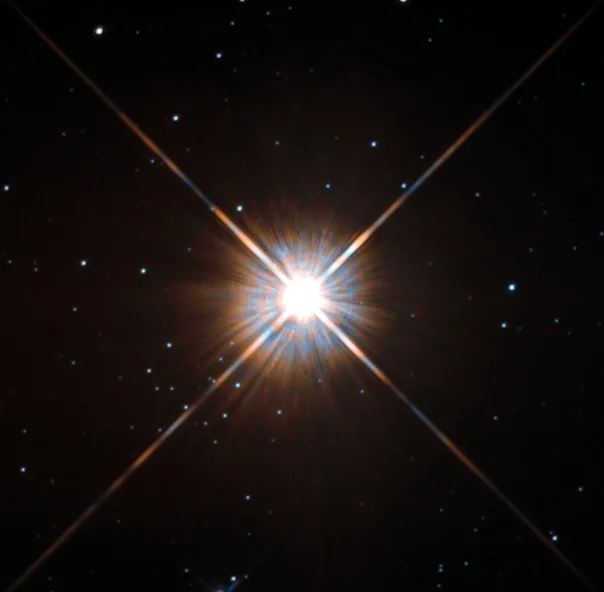 A bright reddish-white star with four long diffraction spikes, surrounded by fainter stars on a black sky.