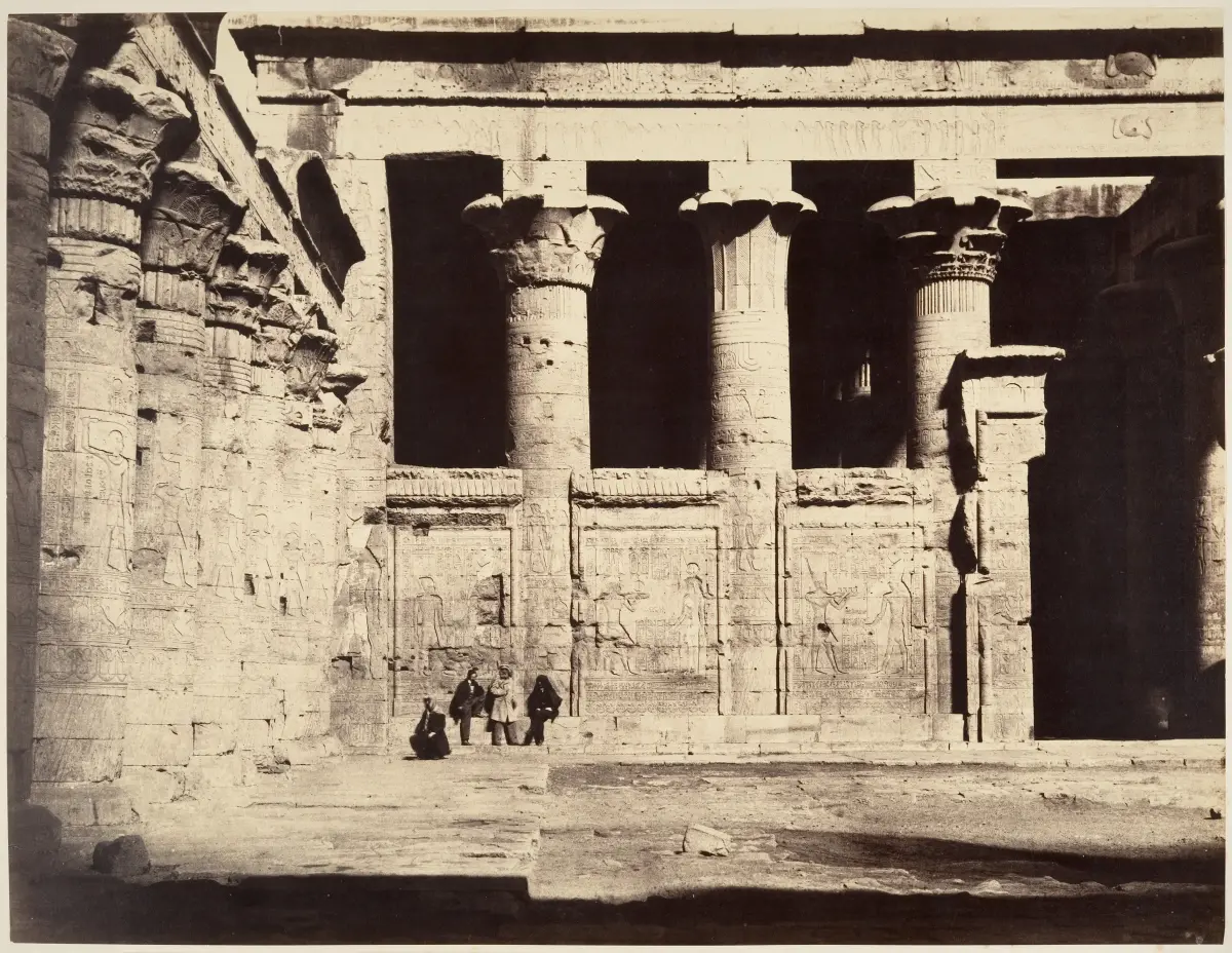 The same temple court with its floor clear, carved panels fully exposed and four men sitting at the foot of the wall.