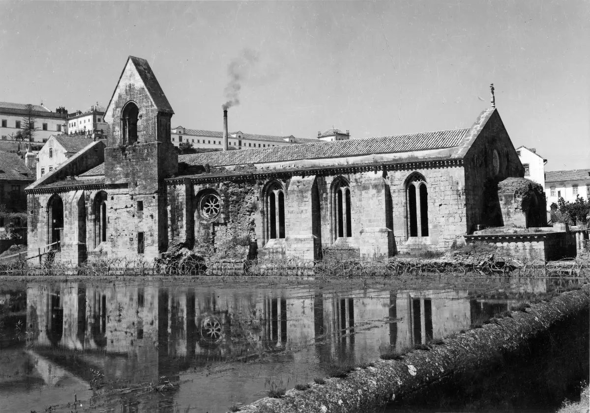 A long Gothic church in black and white with its windows close above a sheet of still water.