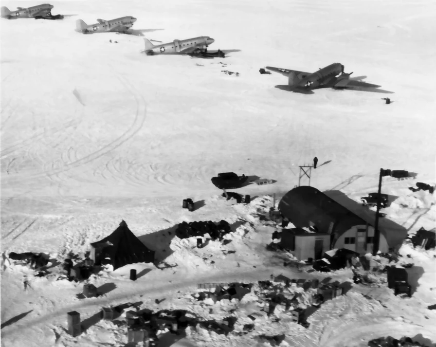 Twin-engine R4D transports on skis lined up on the snow above the huts and tents of Little America IV.