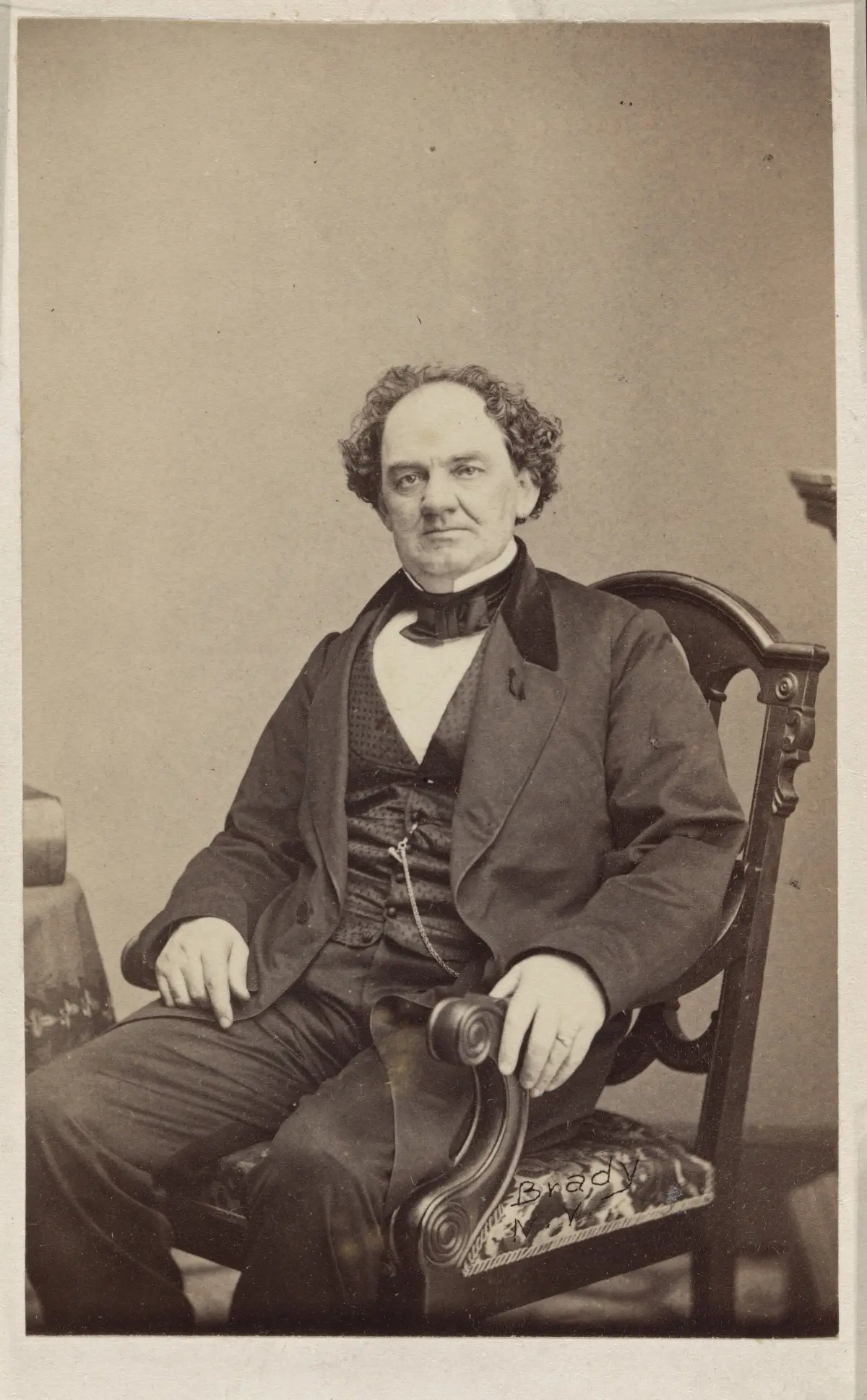 An old studio photograph of a heavy-set man with curly hair in a dark suit, seated.