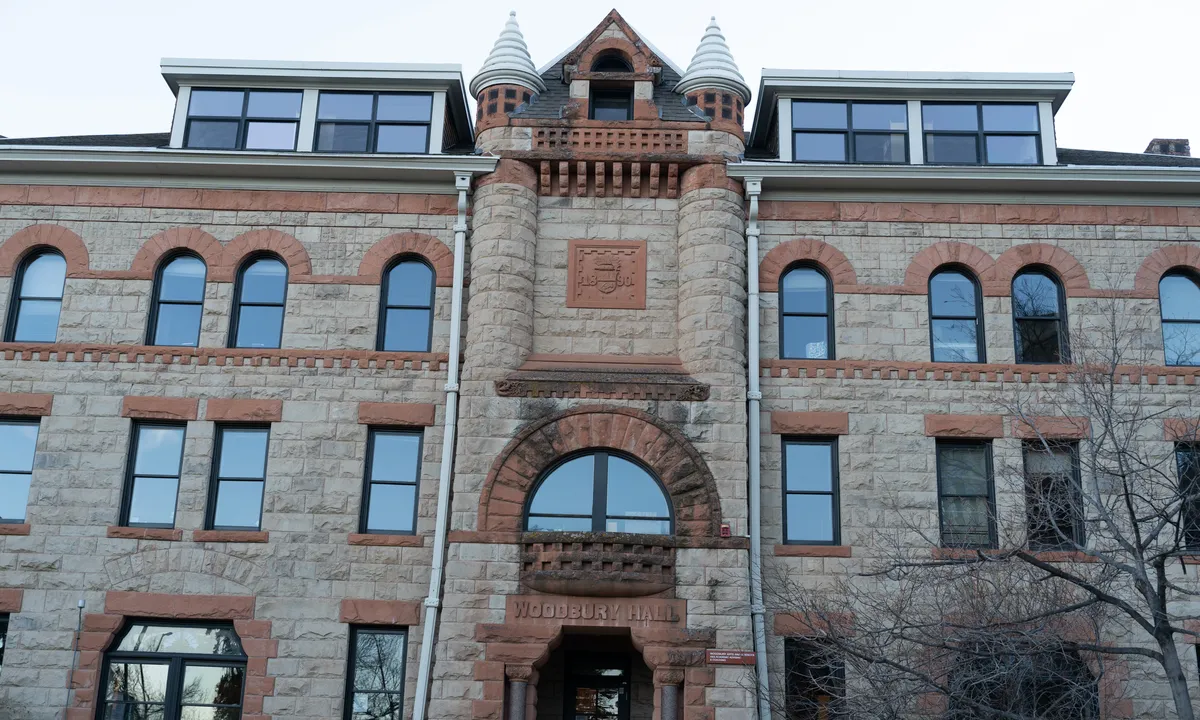 The front of a four-storey sandstone building with red stone arches, a central tower bay with two small turrets and an arched doorway carved with the words Woodbury Hall.