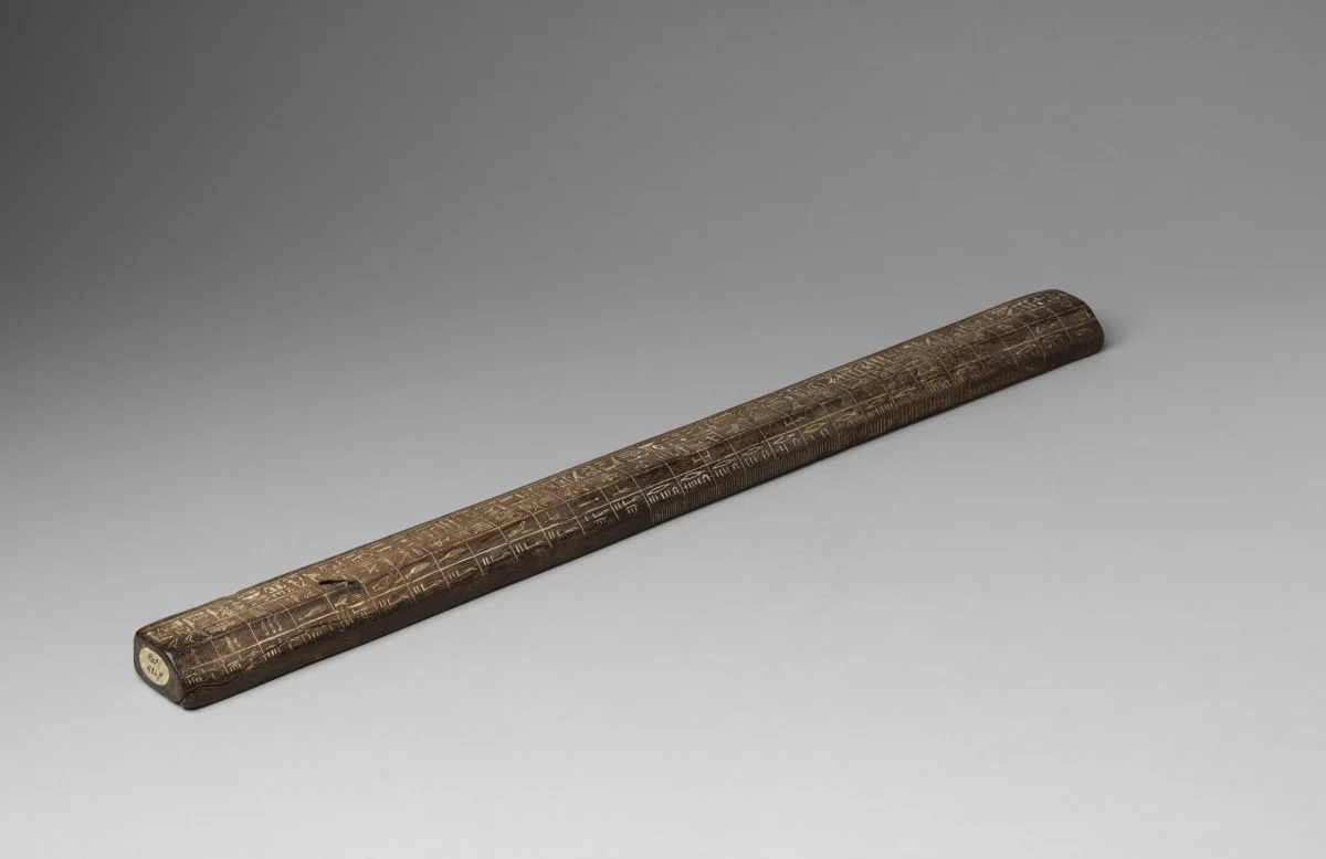 A long dark wooden rod, seen at a slant, lying on a grey ground.