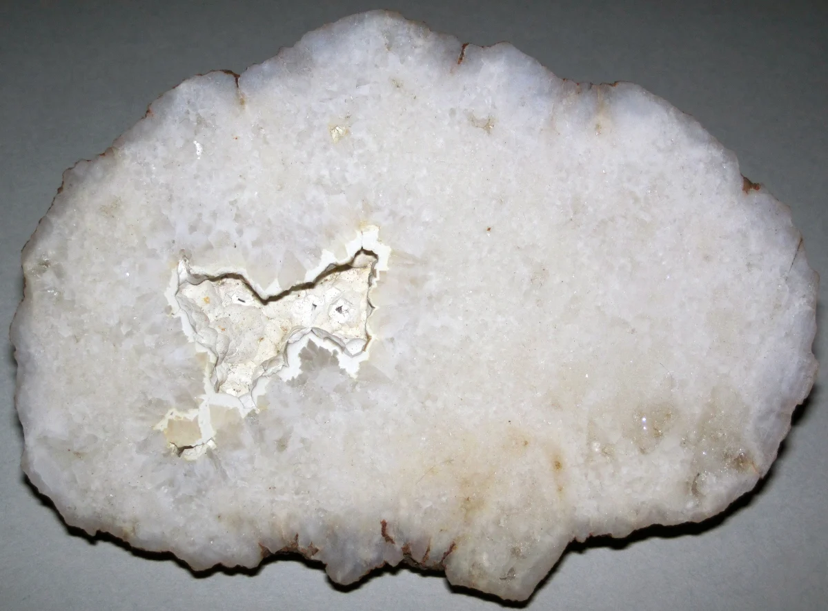 A cut and polished stone, mostly milky white quartz and chalcedony, with a small crystal-lined hollow near its centre.