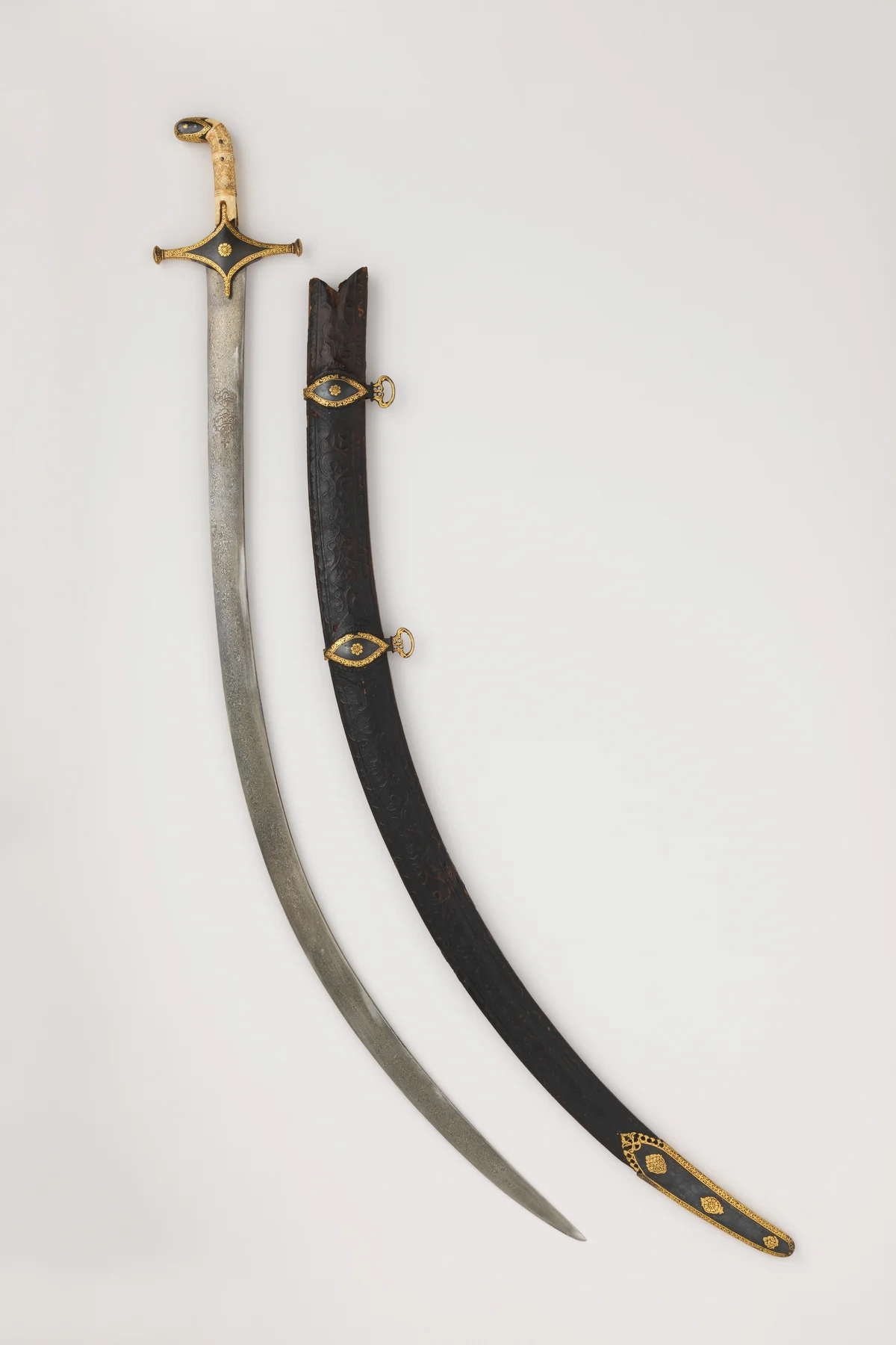 A curved Persian sabre with a gold-mounted hilt and a pale steel blade, shown upright beside its dark leather scabbard with gold fittings.