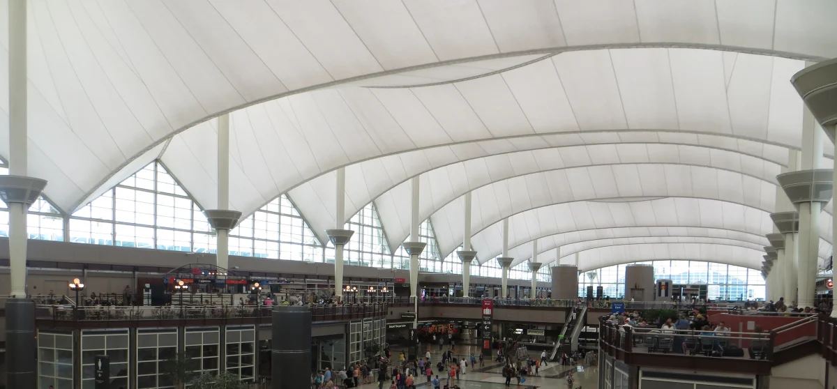 A vast indoor hall with white fabric vaults running away overhead, tall masts, glass end walls and travellers on two levels.