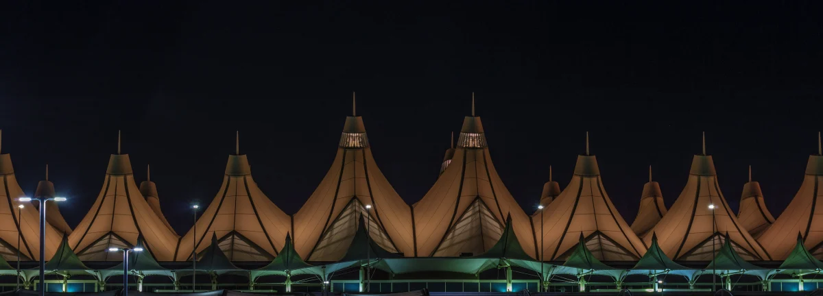 A long row of peaked roofs lit amber against a black sky, with green lit canopies along the roadway beneath.