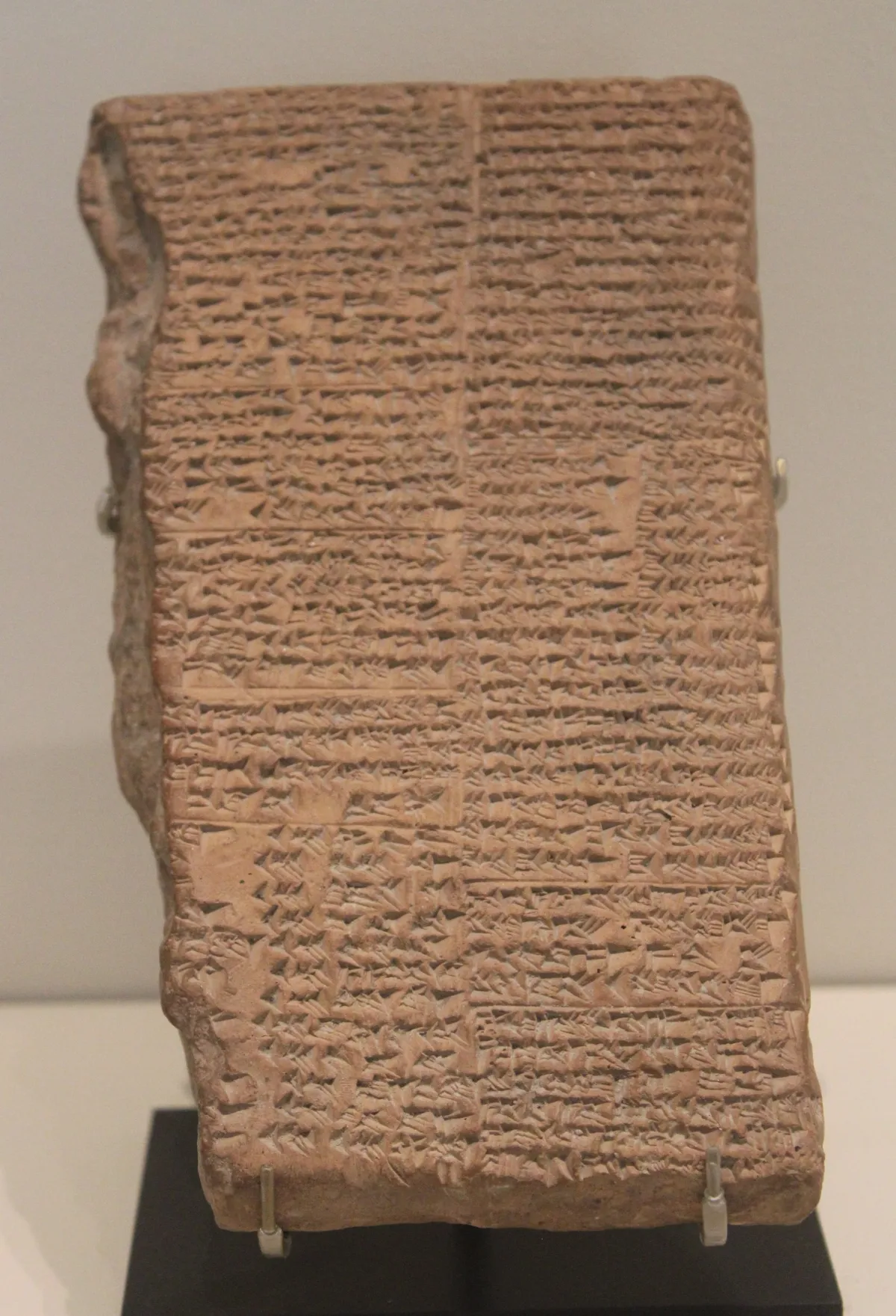 A large rectangular clay tablet densely written in two columns of cuneiform, its corner broken off.