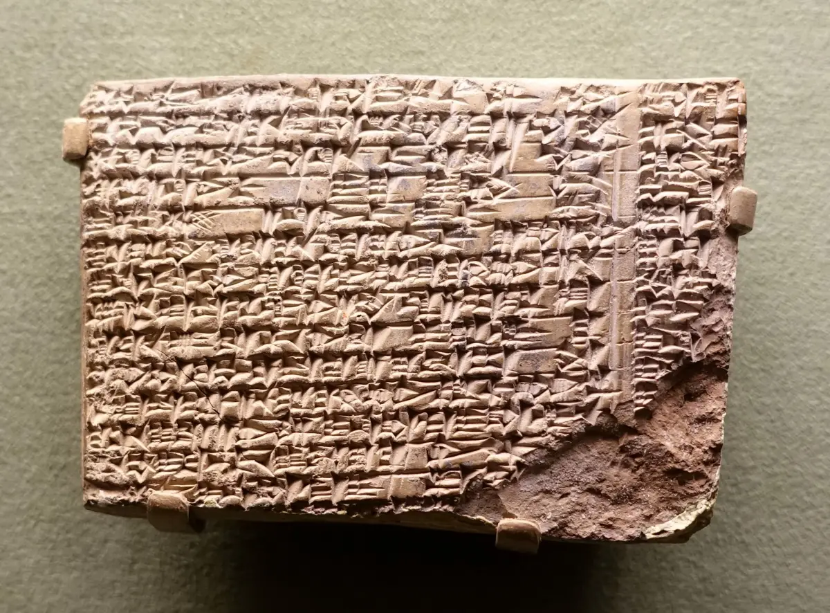 A broken clay tablet densely covered in lines of cuneiform, in a museum case.