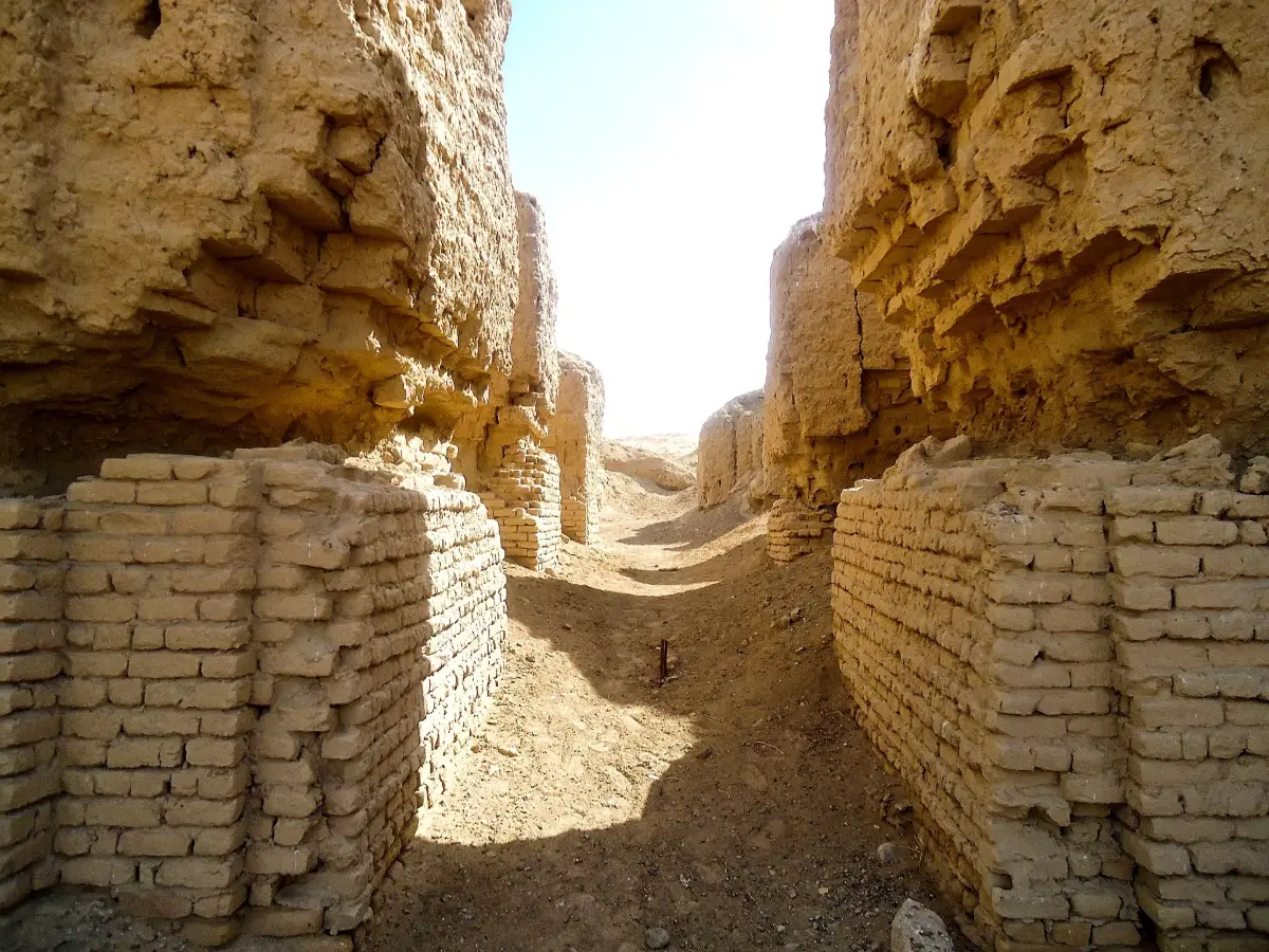 Ruined walls of fired brick in a narrow passage under a pale sky.