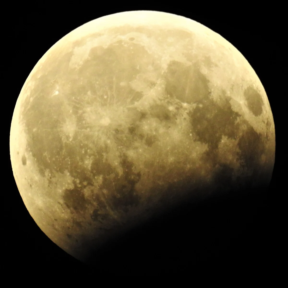 A pale gold full moon with its lower right side sunk in black, the edge of the dark area forming a soft curve.