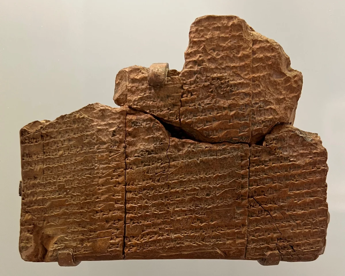 A broken clay tablet, pieced together from fragments, covered in rows of cuneiform signs.