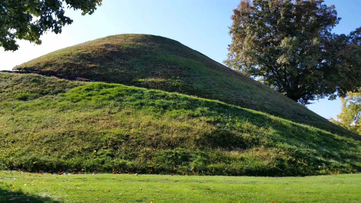A large grass-covered conical mound under a blue sky, with a path around its base.