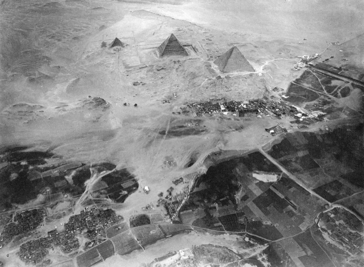 The three pyramids small on the horizon beyond a village and flat fields, photographed from a balloon.