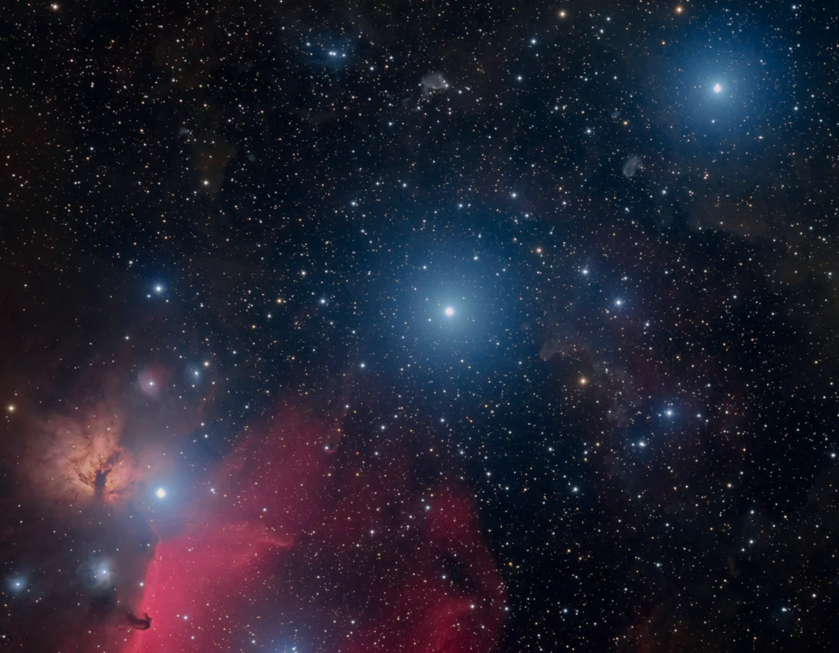 Three bright blue-white stars on a rising diagonal across a field of faint stars, with red and brown nebulae at lower left.