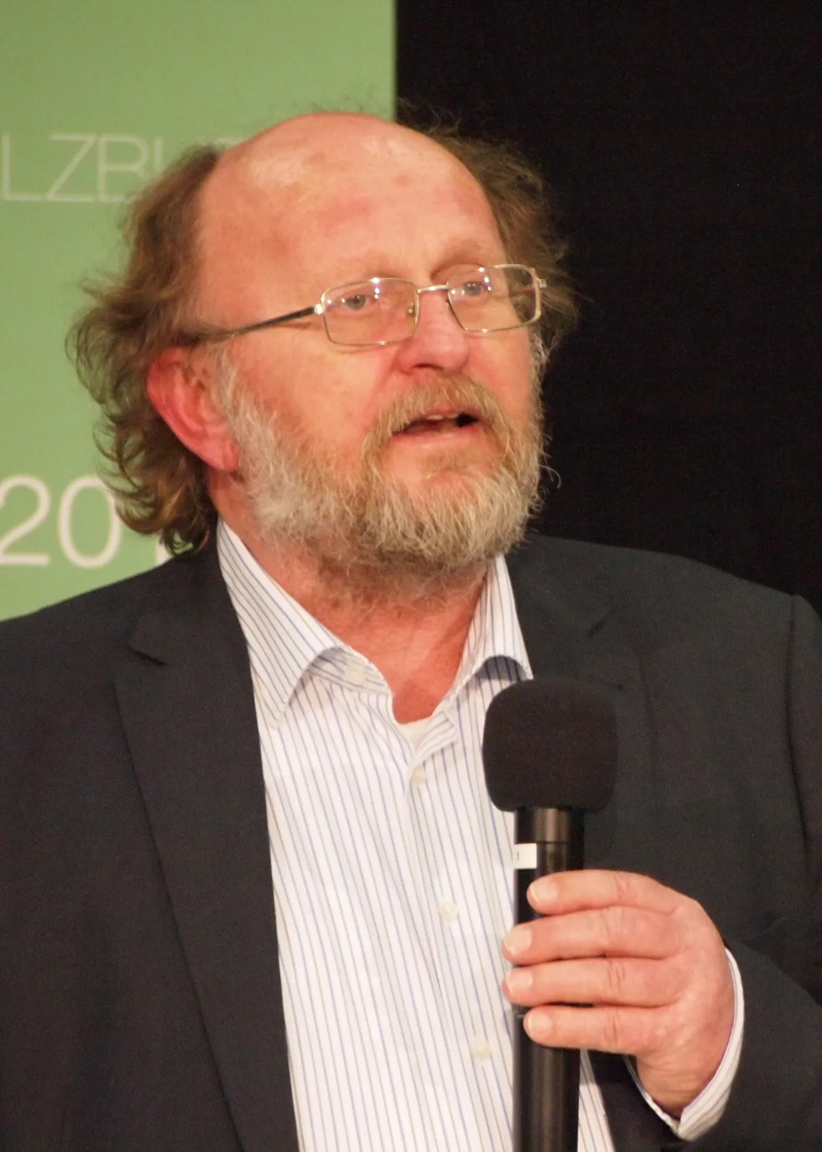 A bearded man with glasses speaking into a microphone.