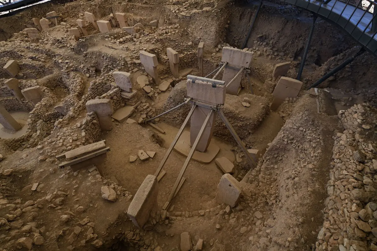 A ring of upright stone pillars in an excavation pit, two large T-shaped pillars braced with timber at the centre.