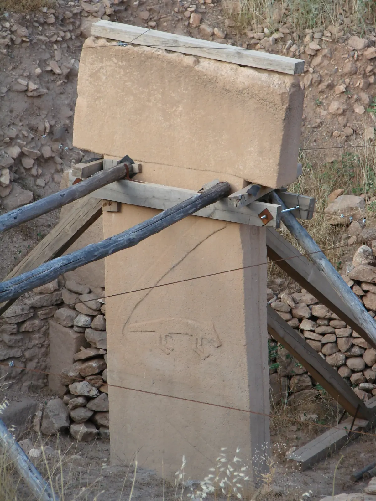 A tall T-shaped stone pillar braced with timbers, a carved arm and a fox in relief on its side.