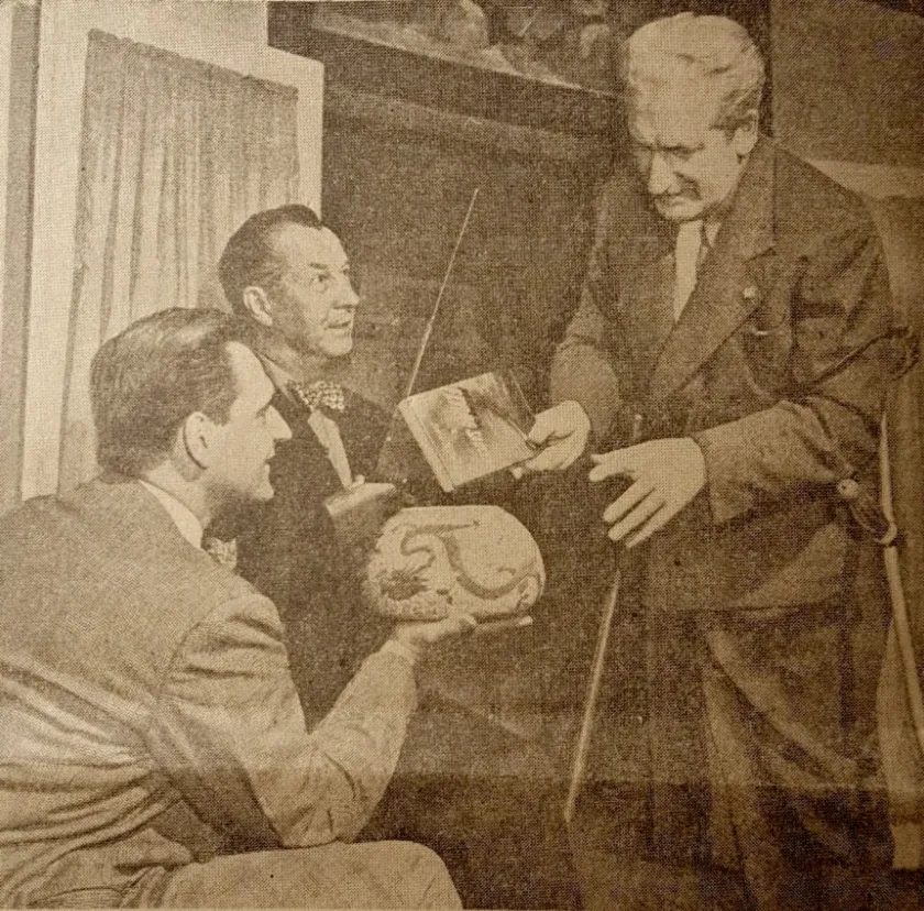 Three men in suits in a 1950 newspaper photograph: George Koehler holds an upturned bowl standing for the Earth, Silas Newton stands behind him, and Frank Scully holds a book out like a flying saucer