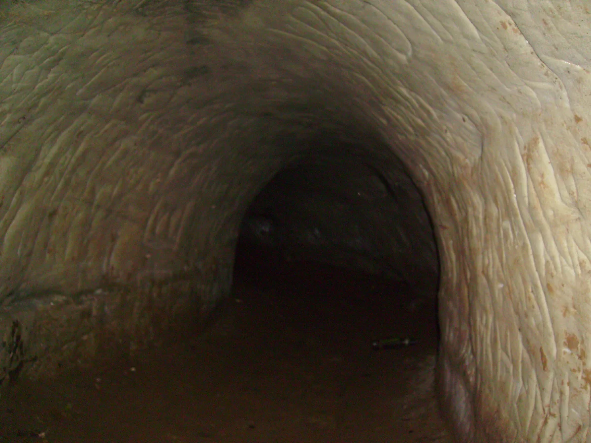 A low arched tunnel in pale sandstone, its walls scored, running into darkness.