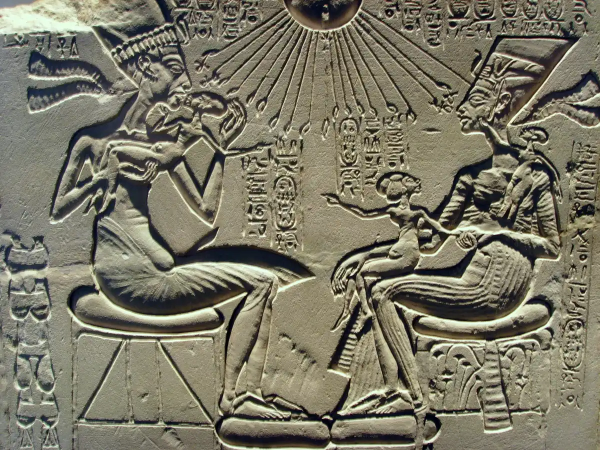 A limestone relief of a seated king and queen holding their children beneath a sun disc with rays.