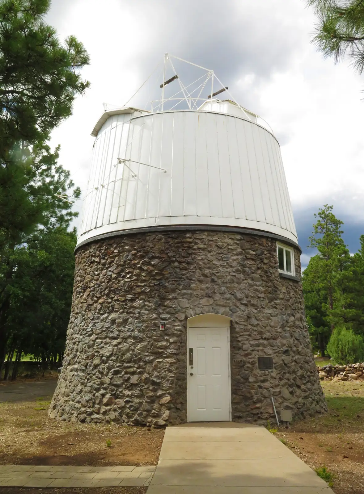 A small observatory among pine trees: a round base of rough stone and a white dome above it