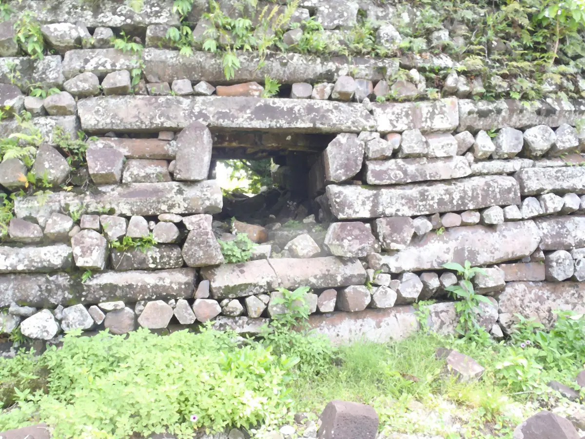 A wall face with a low square opening under a long lintel of basalt, framed by column ends and long columns.