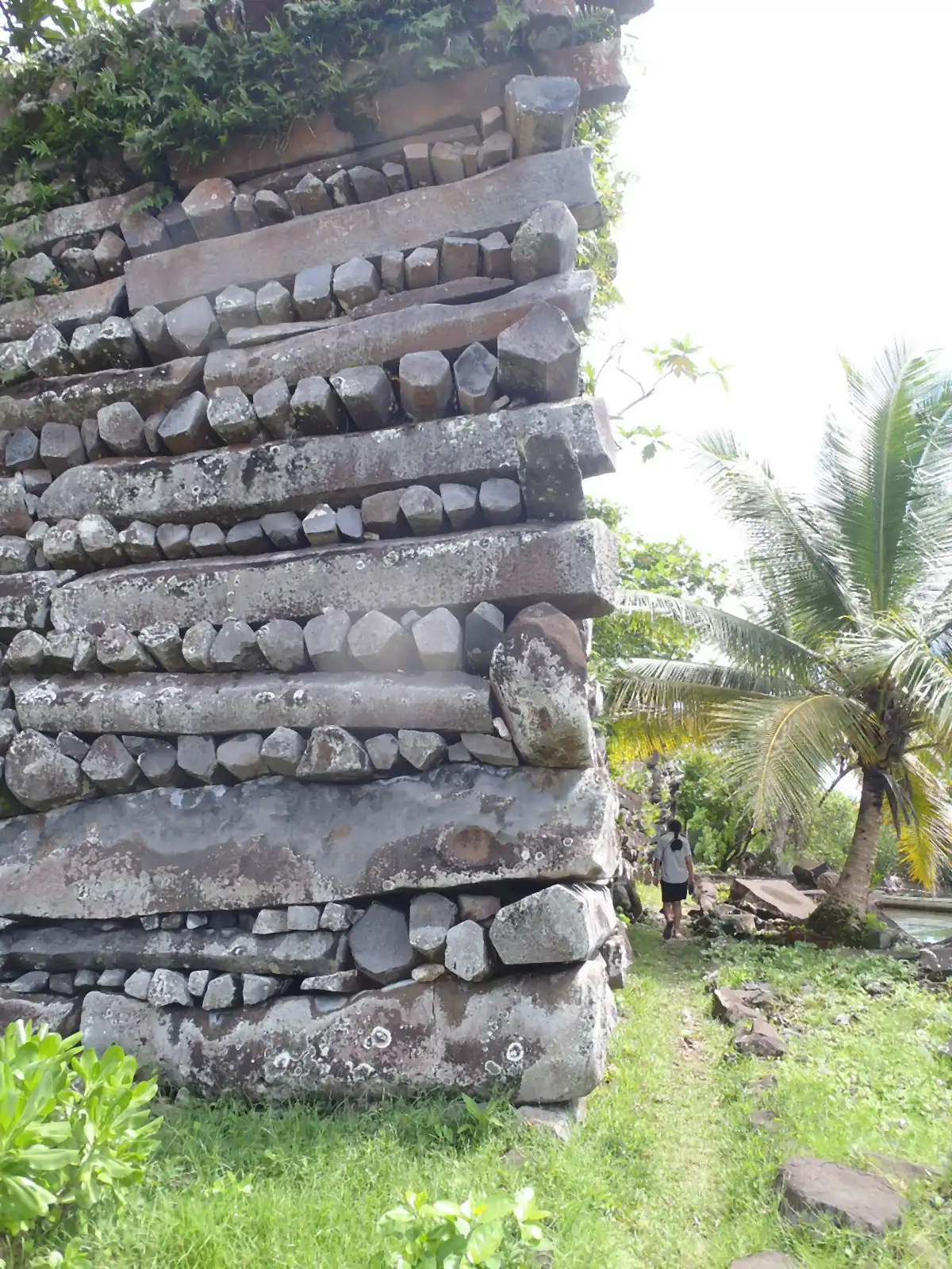 The end of a wall in close view: long basalt columns laid lengthwise alternate with rows of five- and six-sided column ends, with a person walking past at the foot.