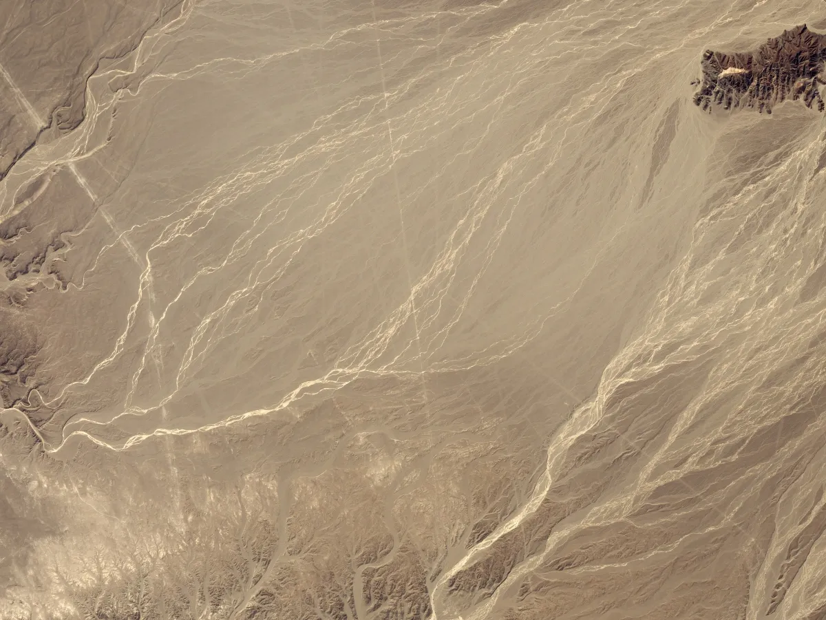 A natural-colour satellite view of pale desert crossed by faint straight lines and dry streambeds.