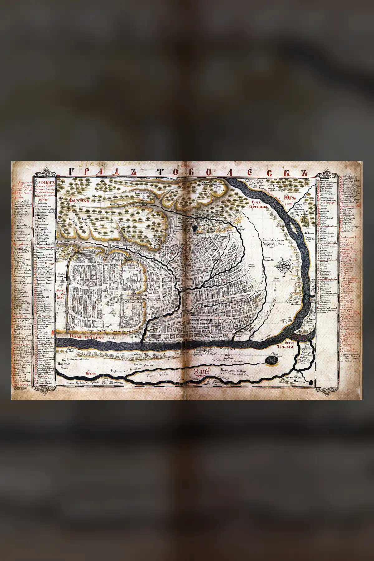 A hand-drawn plan of Tobolsk from 1701, with rivers in black, the walled town and street grid, and numbered lists down both sides, set on a dark blurred copy of itself.