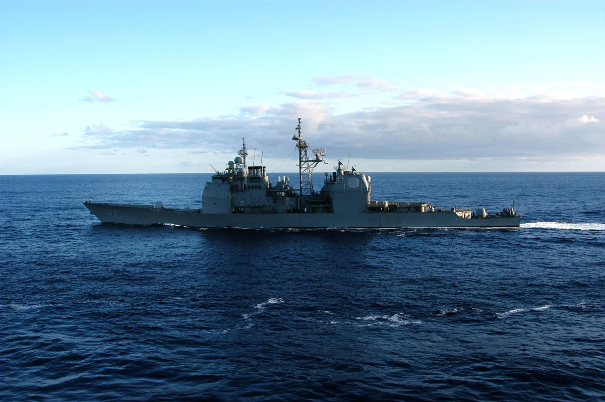 A grey guided-missile cruiser with a tall square superstructure steams across a dark blue sea under a pale sky.