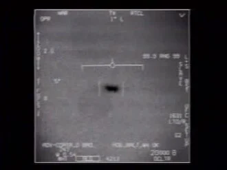 A grey infrared camera frame with targeting symbols and numbers around the edges; a small dark oblong shape sits just below the centre crosshair.