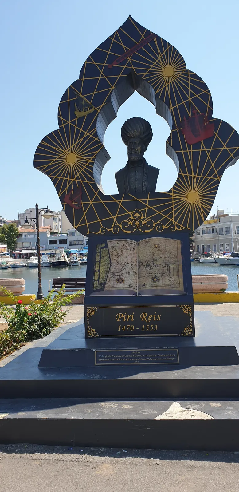 A monument to Piri Reis on the waterfront at Gelibolu: a bust in a turban inside a gilded frame of compass lines, above an open book of maps and the dates 1470-1553.