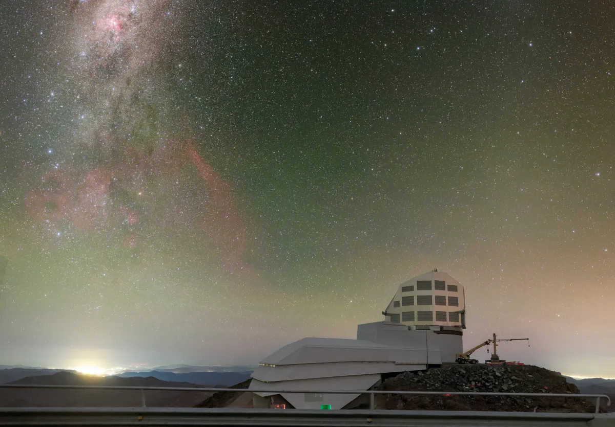 The Rubin Observatory's white dome on a mountain ridge at night, under the bright band of the Milky Way.