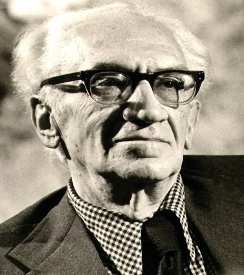 Black and white portrait of an old man with white hair, heavy dark glasses, a check shirt and a dark tie