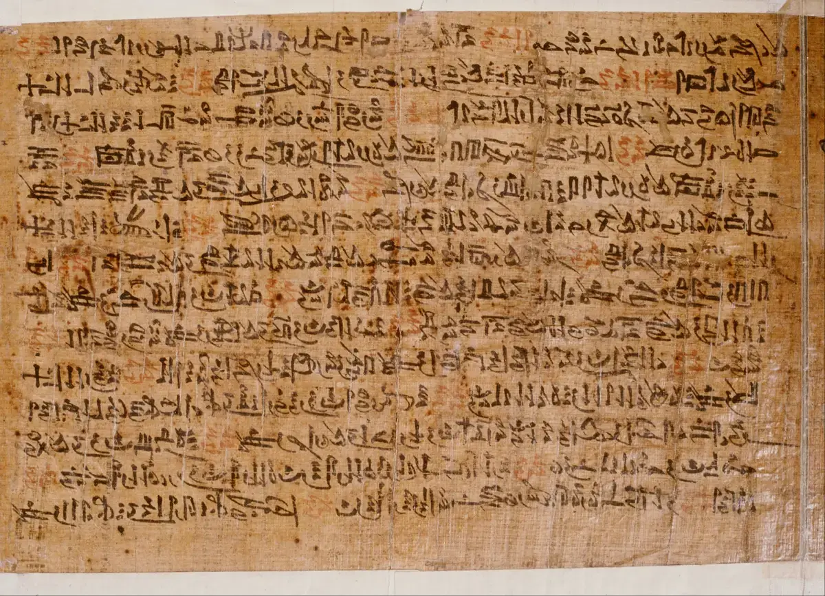 A page of brown papyrus covered in close lines of black hieratic script with a few words in red