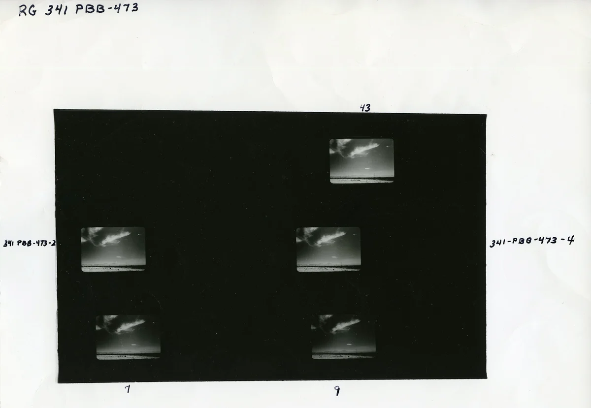 A black mounting card on white paper holding five small film frames, each showing clouds over a flat horizon with a bright elongated speck in the sky, with handwritten catalogue numbers.