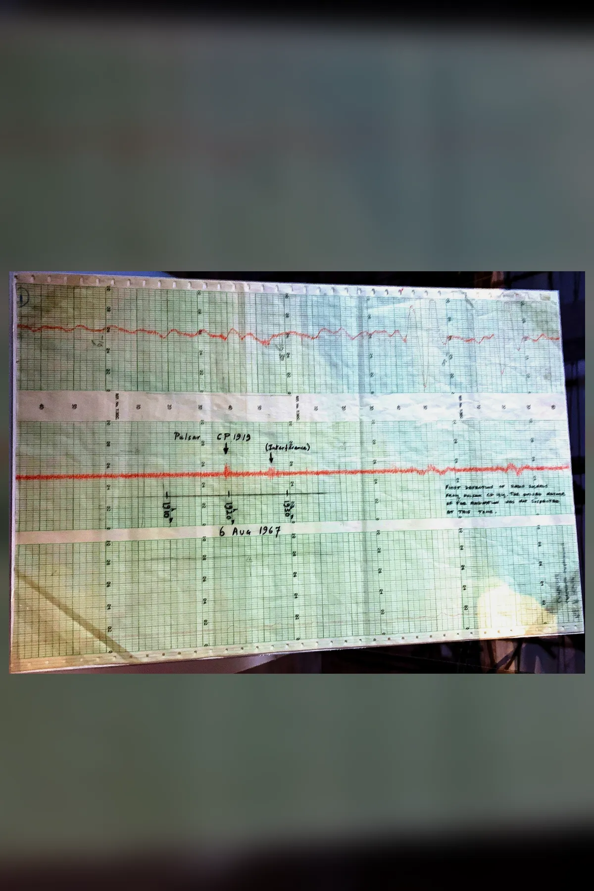 A strip of green chart paper with two red pen traces. On the lower trace a small spike is labelled Pulsar CP 1919, a second spike beside it is labelled Interference, and the date 6 Aug 1967 is written below.